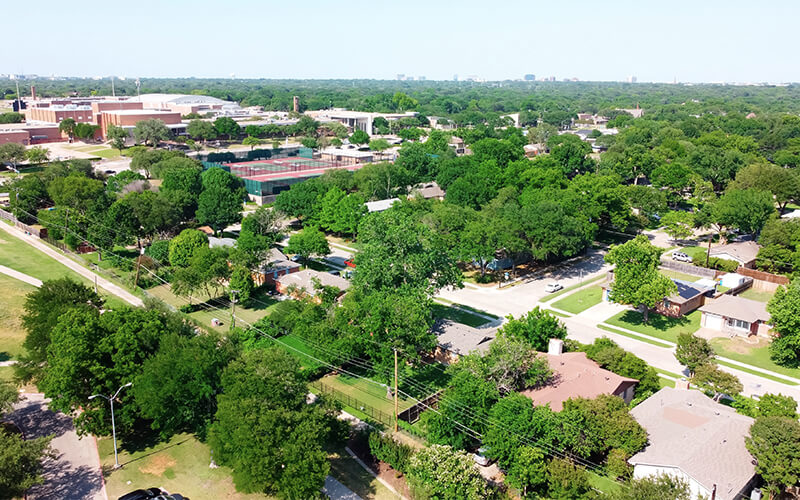 Aerial view of residential neighborhood near sports complex with park, tennis court, stadium in Richardson, Texas, USA. Establishment of a subdivision with lush trees and downtown Dallas in the background